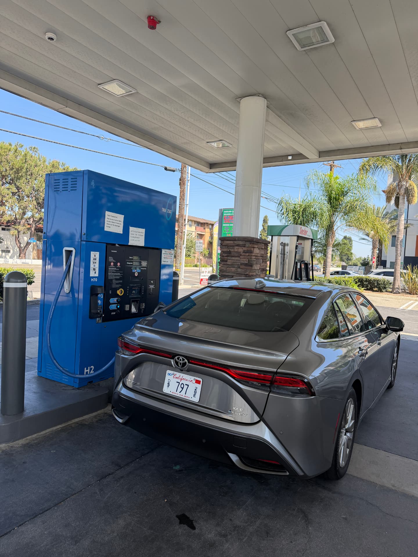 A gray Toyota Mirai parked at a blue True Zero hydrogen fueling station under a gas station canopy