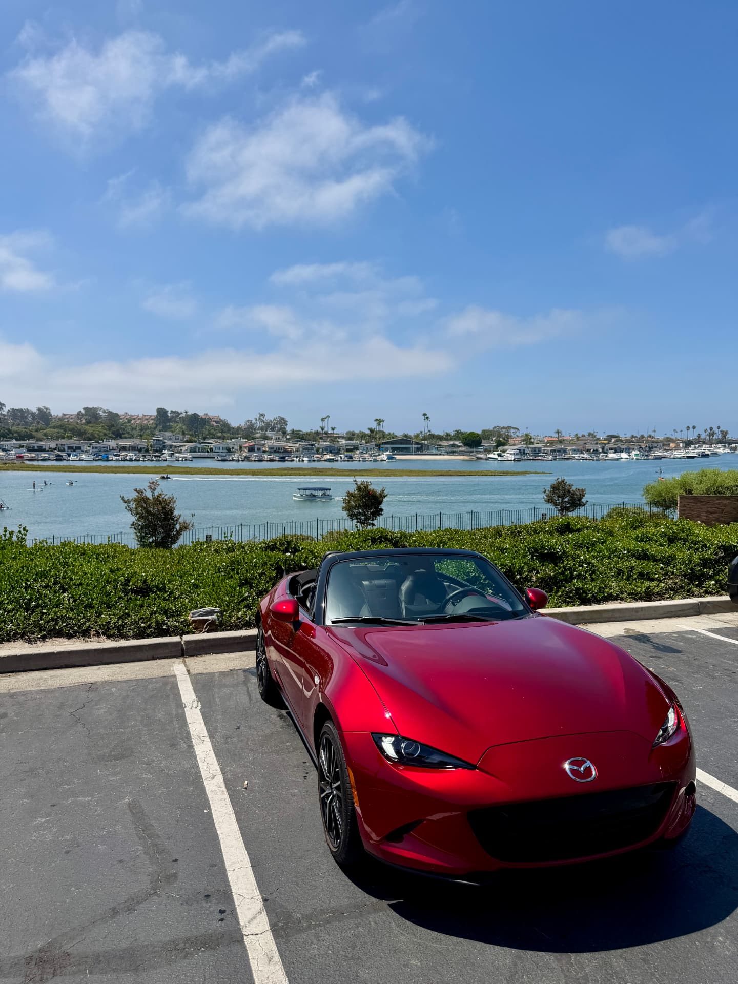 Red Mazda Miata parked beside a sunny harbor with its top down